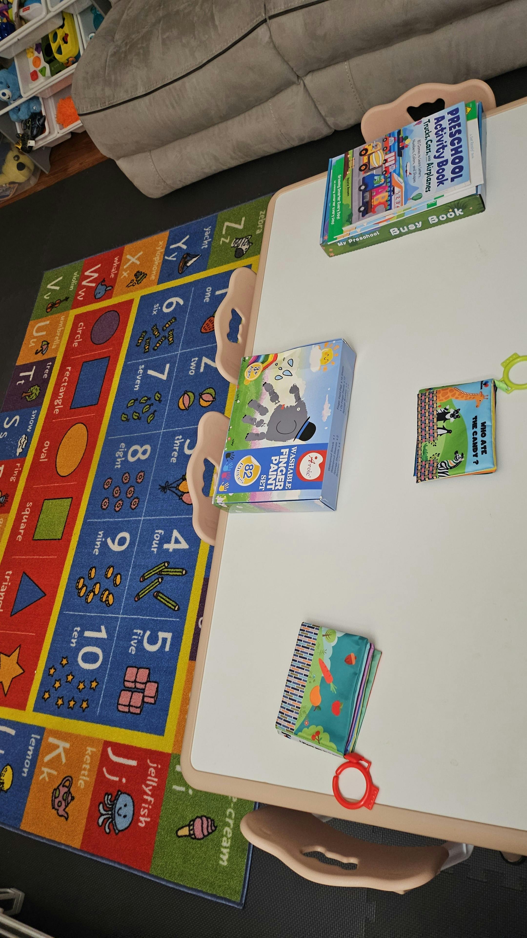 Children's activity books on a white table next to an alphabet rug