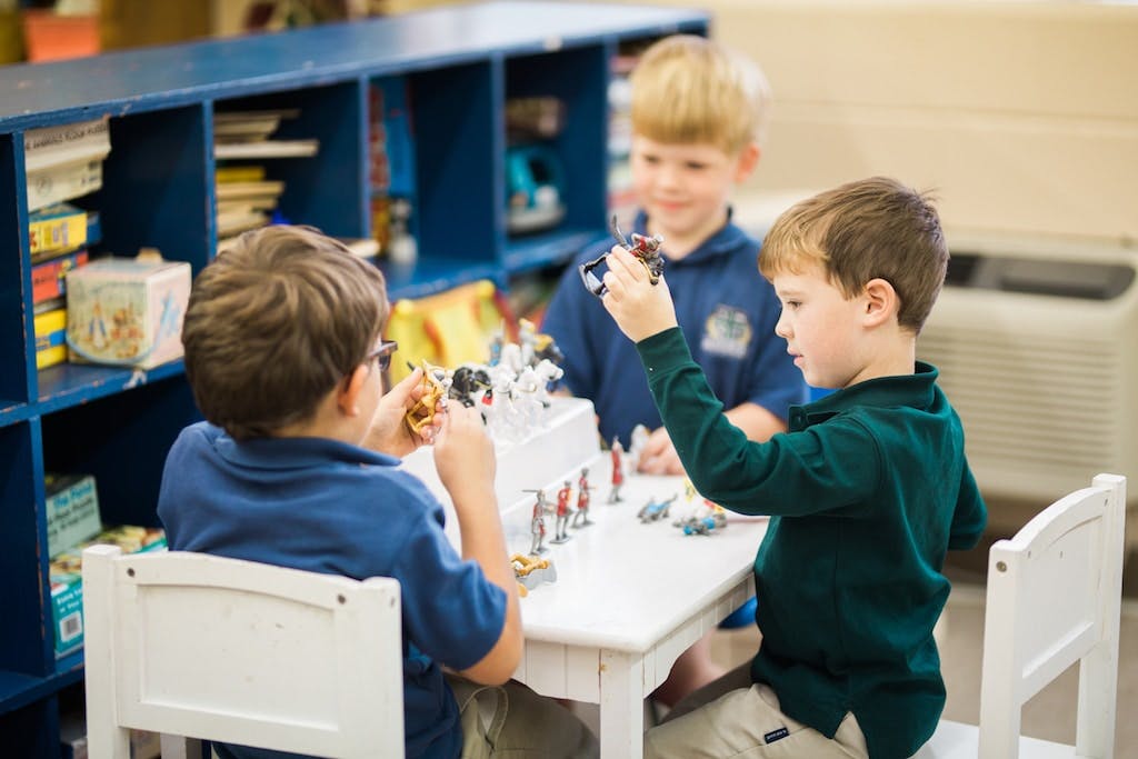 Three children playing with small toys at a table
