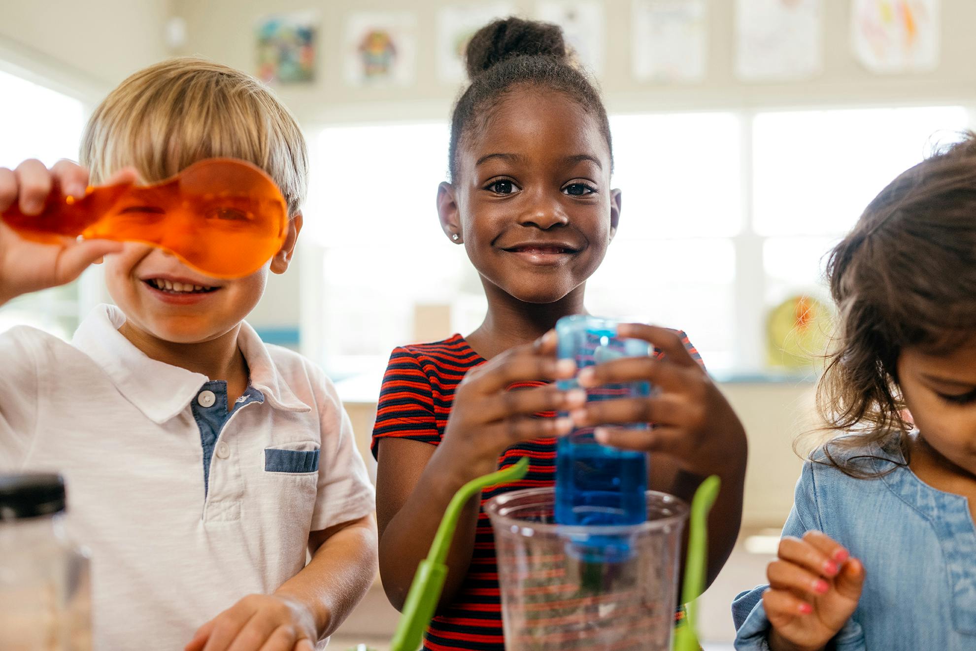 Child holding orange magnifying glass, child holding blue bottle over beaker