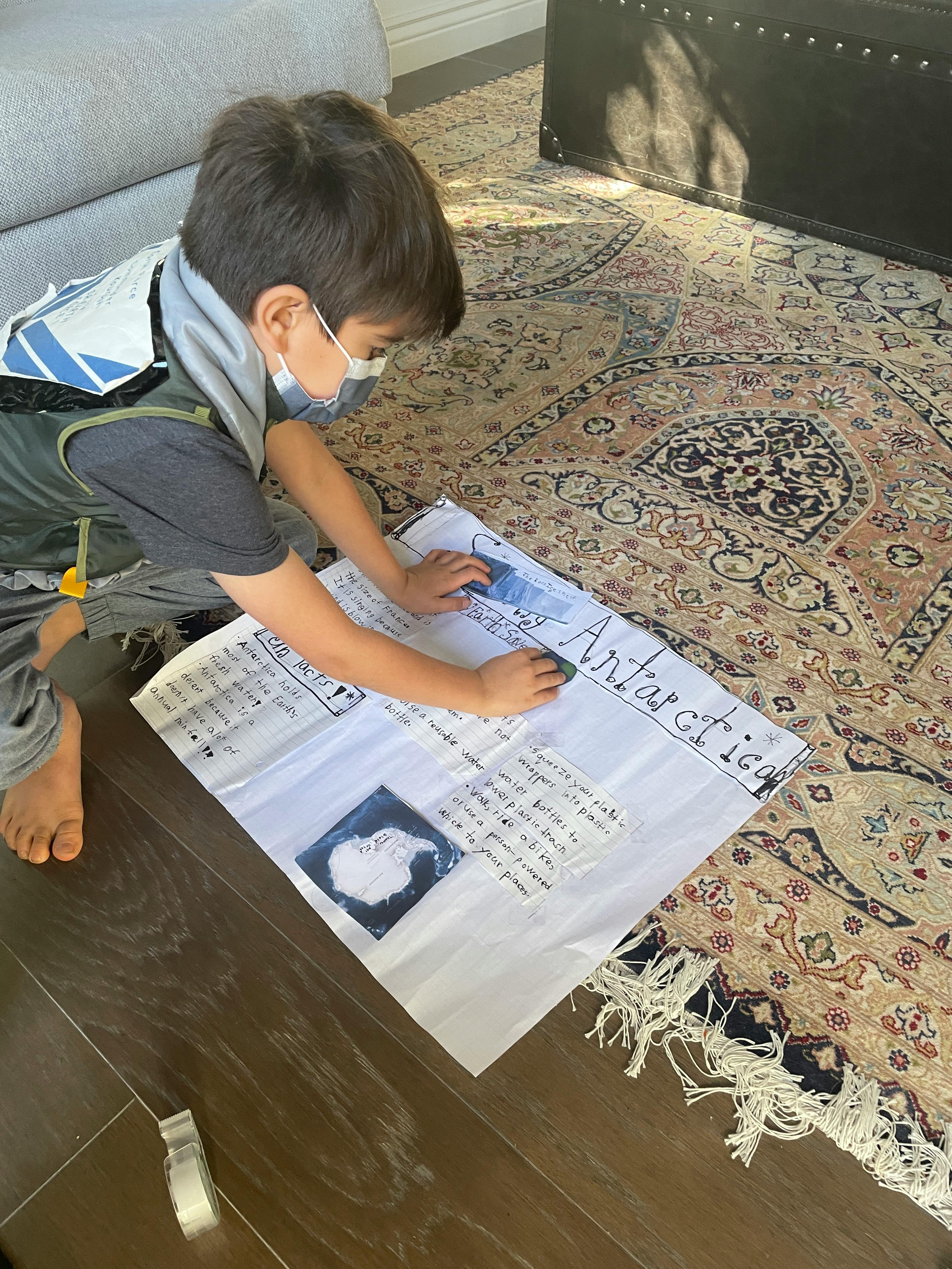 Child in a face mask working on a poster board on the floor