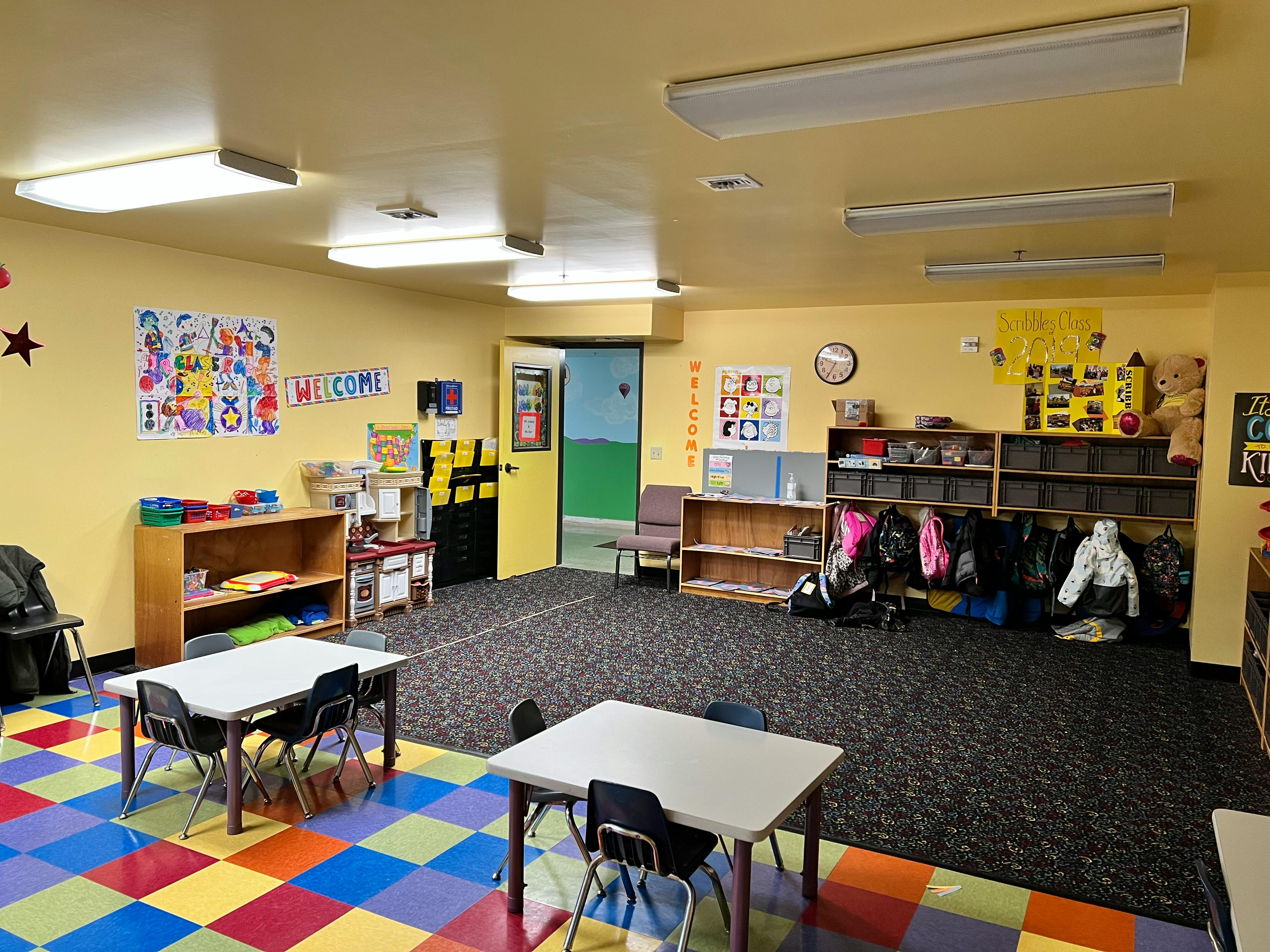 Classroom with small tables and chairs, shelves, and colorful floor tiles