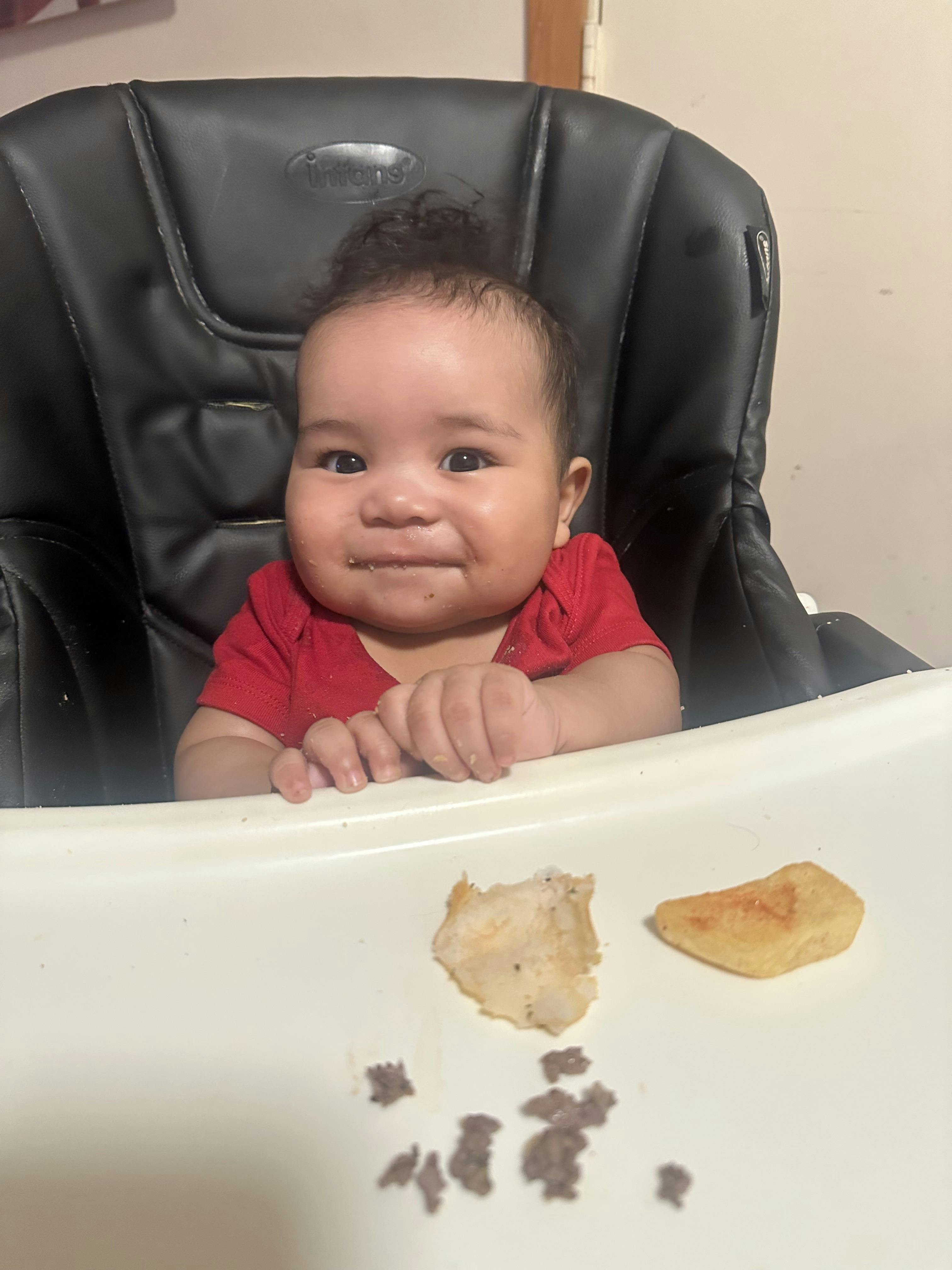Child in a high chair with food around their mouth and on the tray