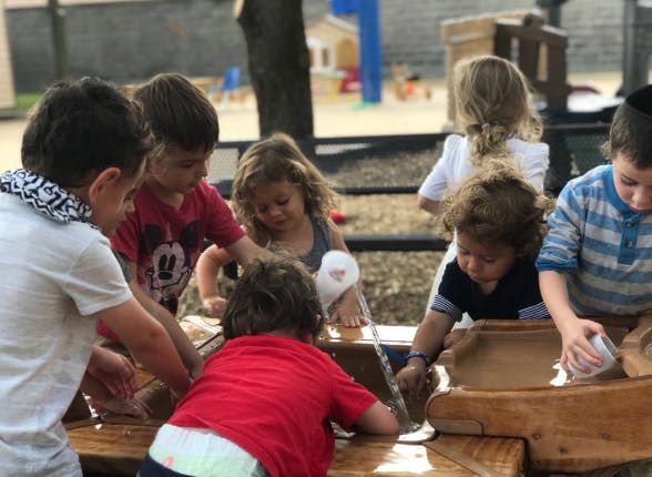 Group of children playing with water at a wooden table