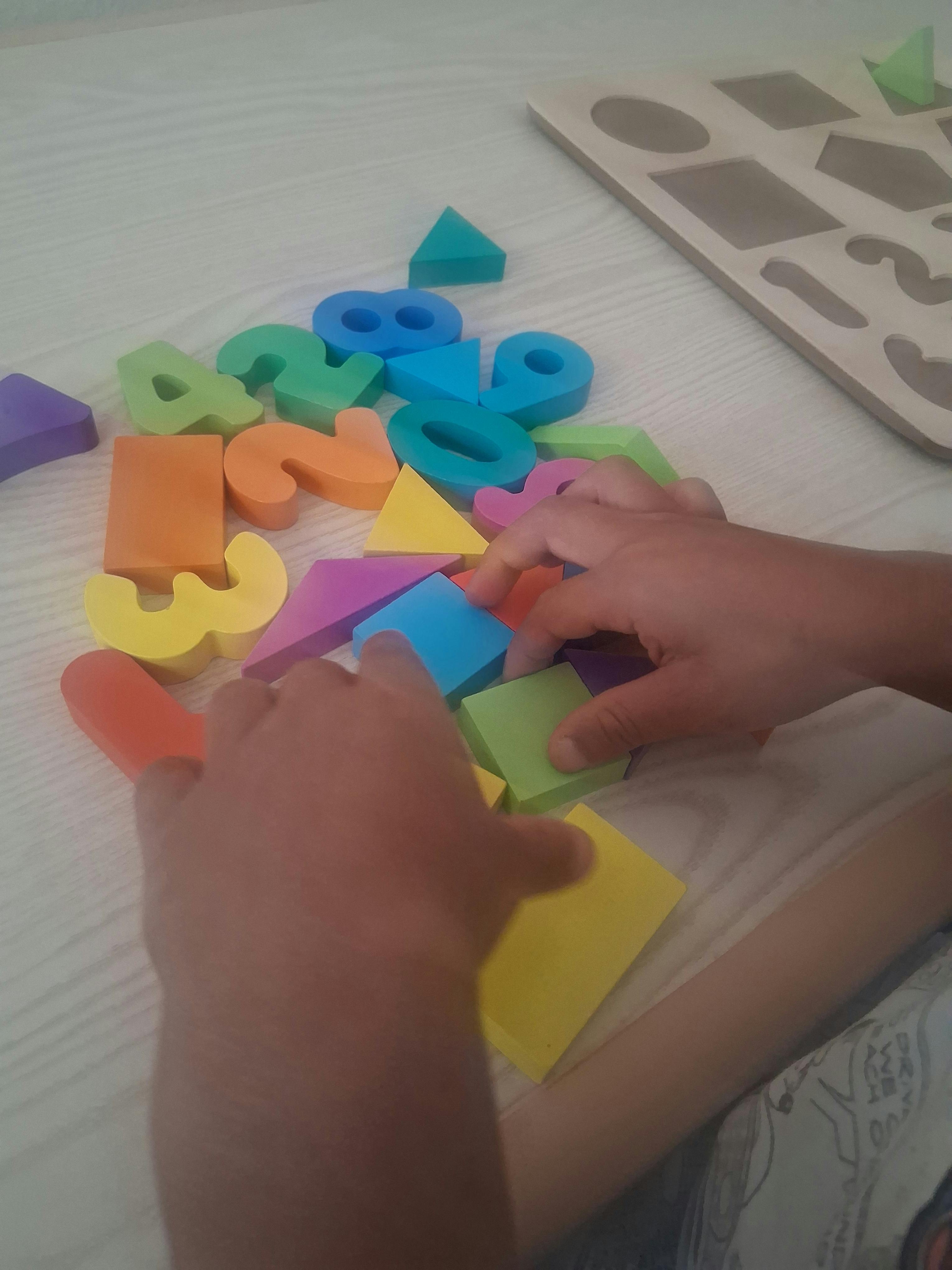 Child's hands sorting colorful foam numbers and shapes