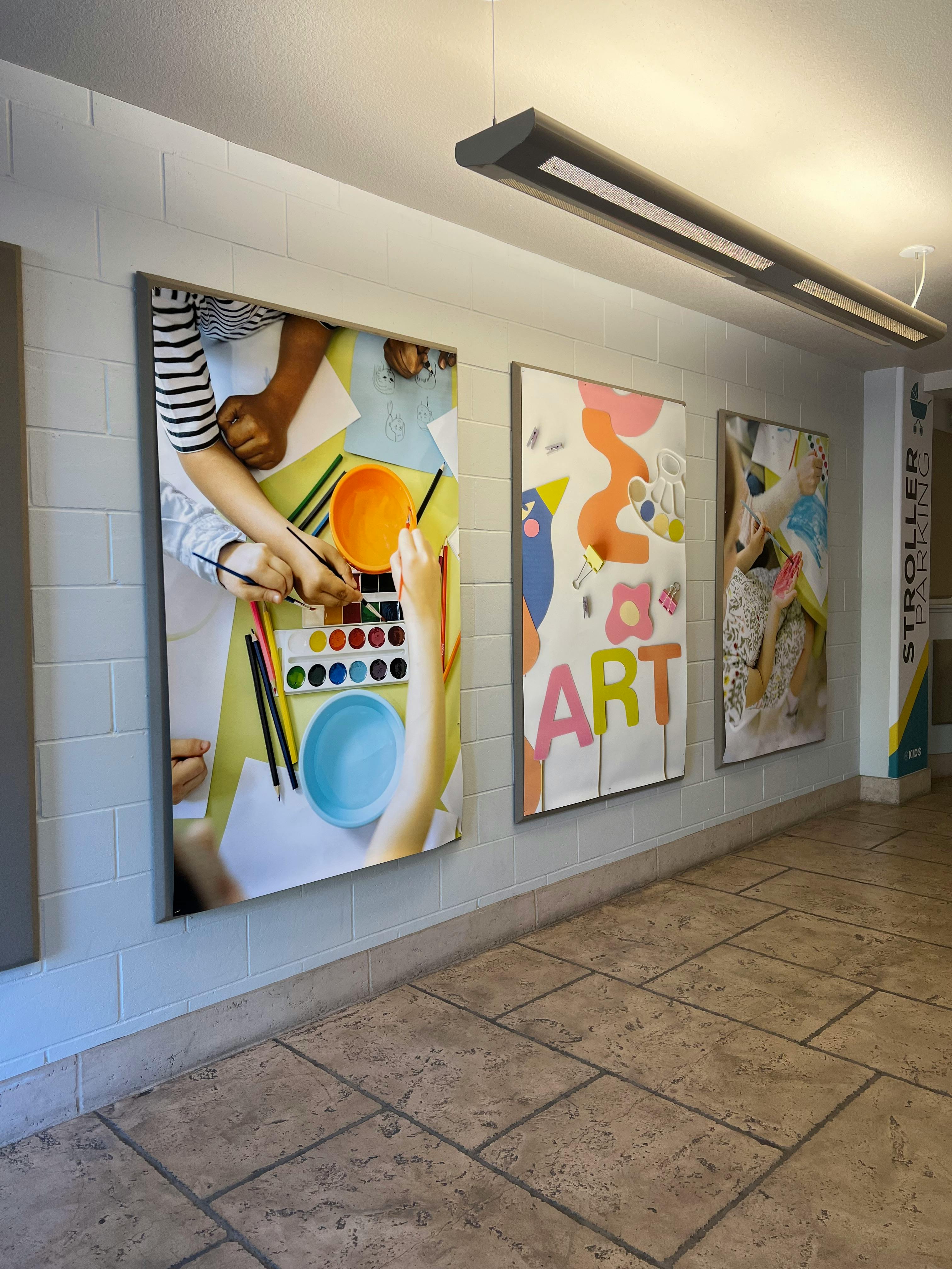 Three large art prints on a white brick wall, one with the word ART