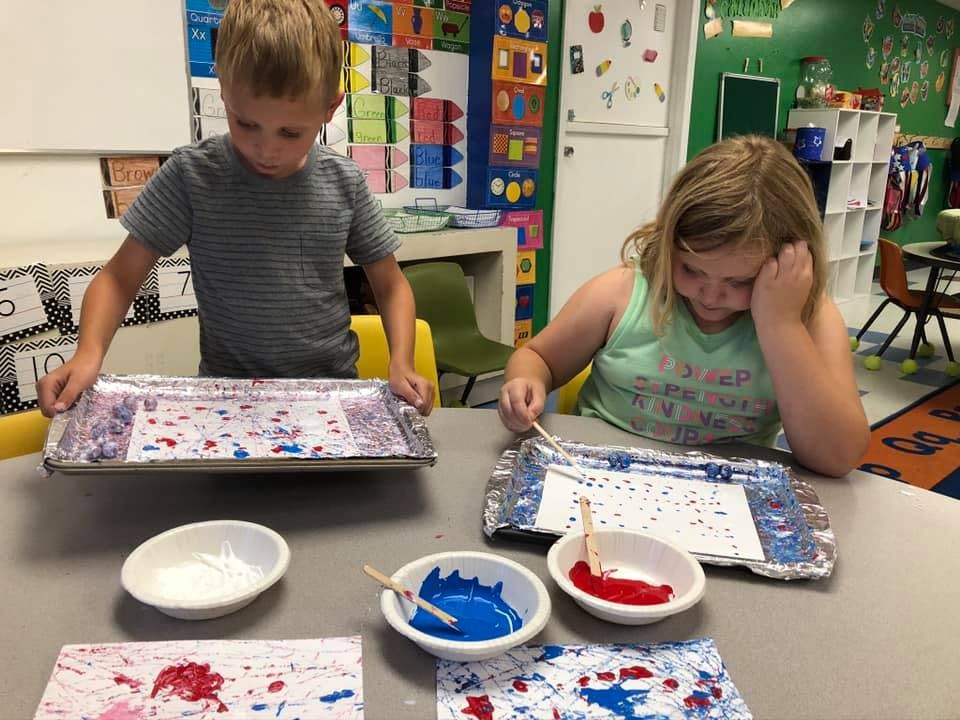 Two children doing art with paint in a classroom