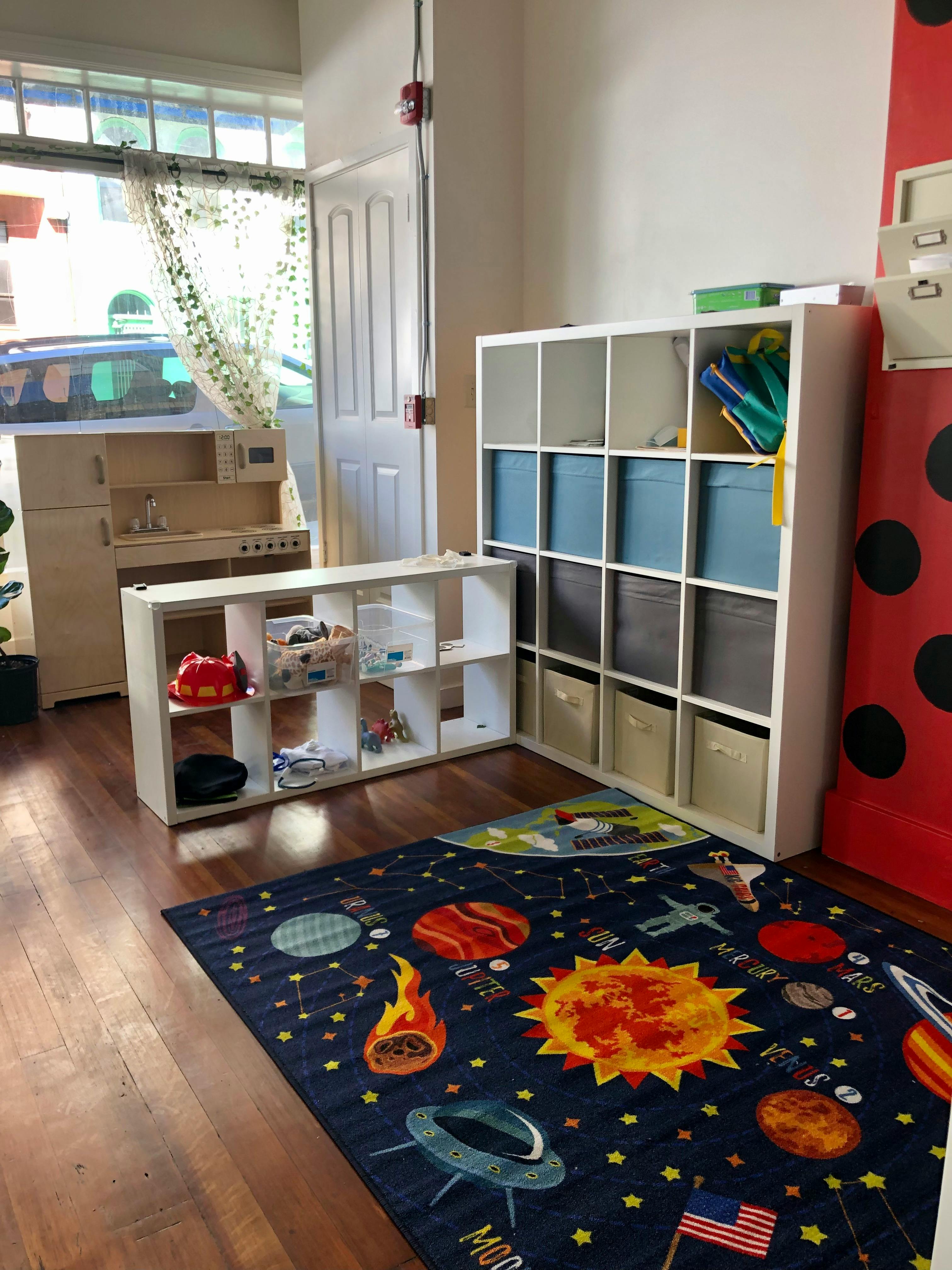 Playroom with toy kitchen, storage shelves, and space-themed rug