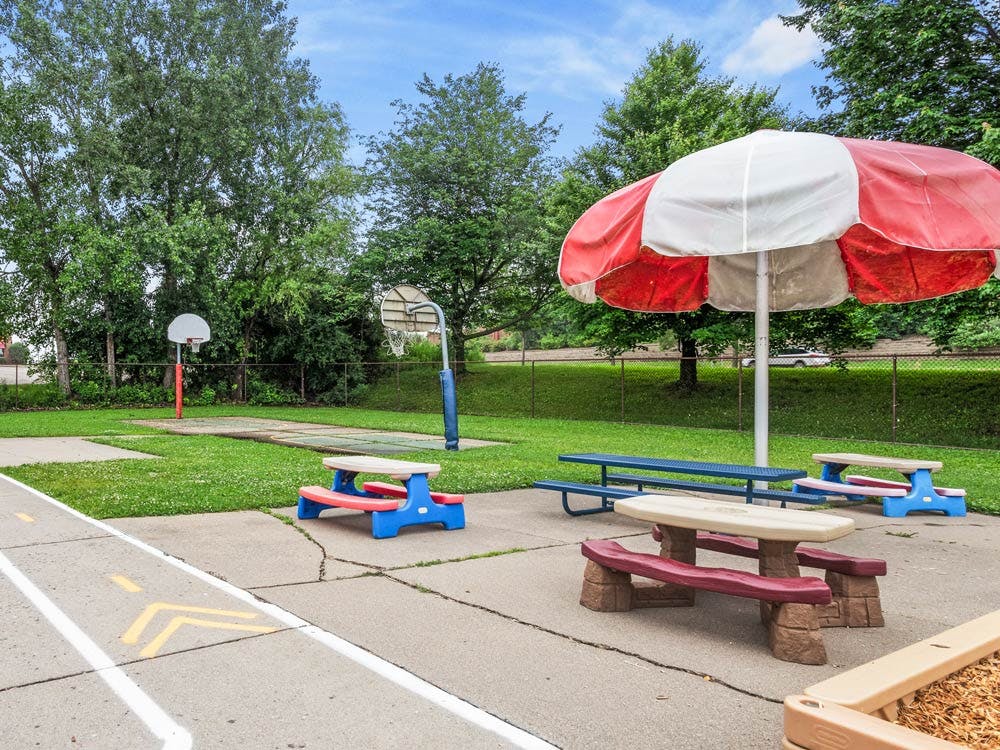 Outdoor area with a red and white umbrella, picnic tables, and basketball hoops