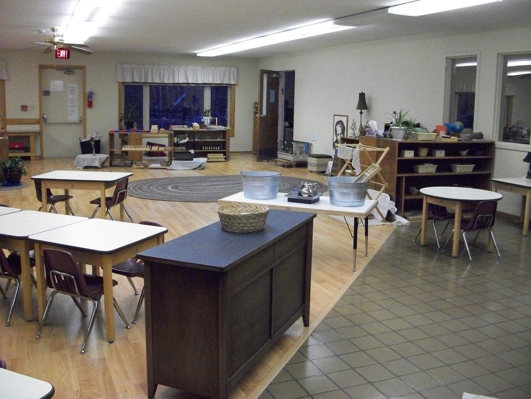 Classroom with small tables and chairs, shelves, and a rug