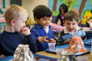 Three children watching a science experiment with a volcano model