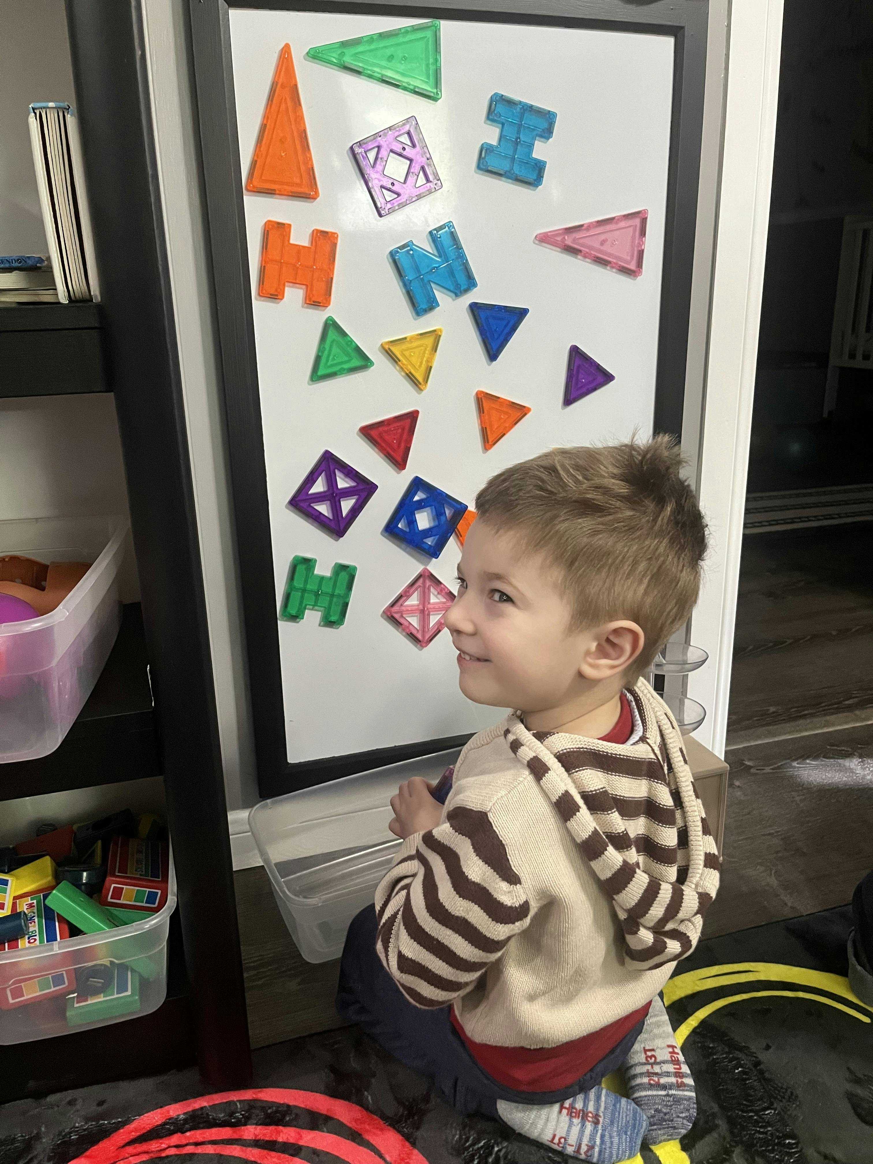 Child playing with magnetic shapes on a whiteboard