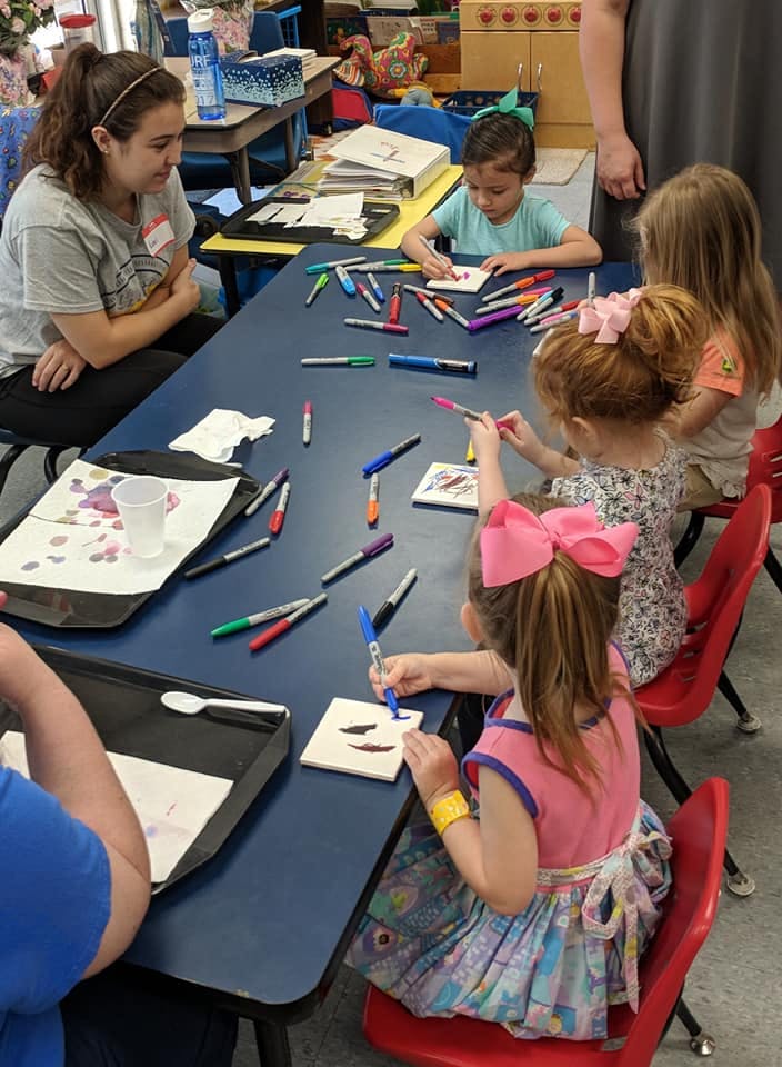 Adult and children drawing with markers at a table