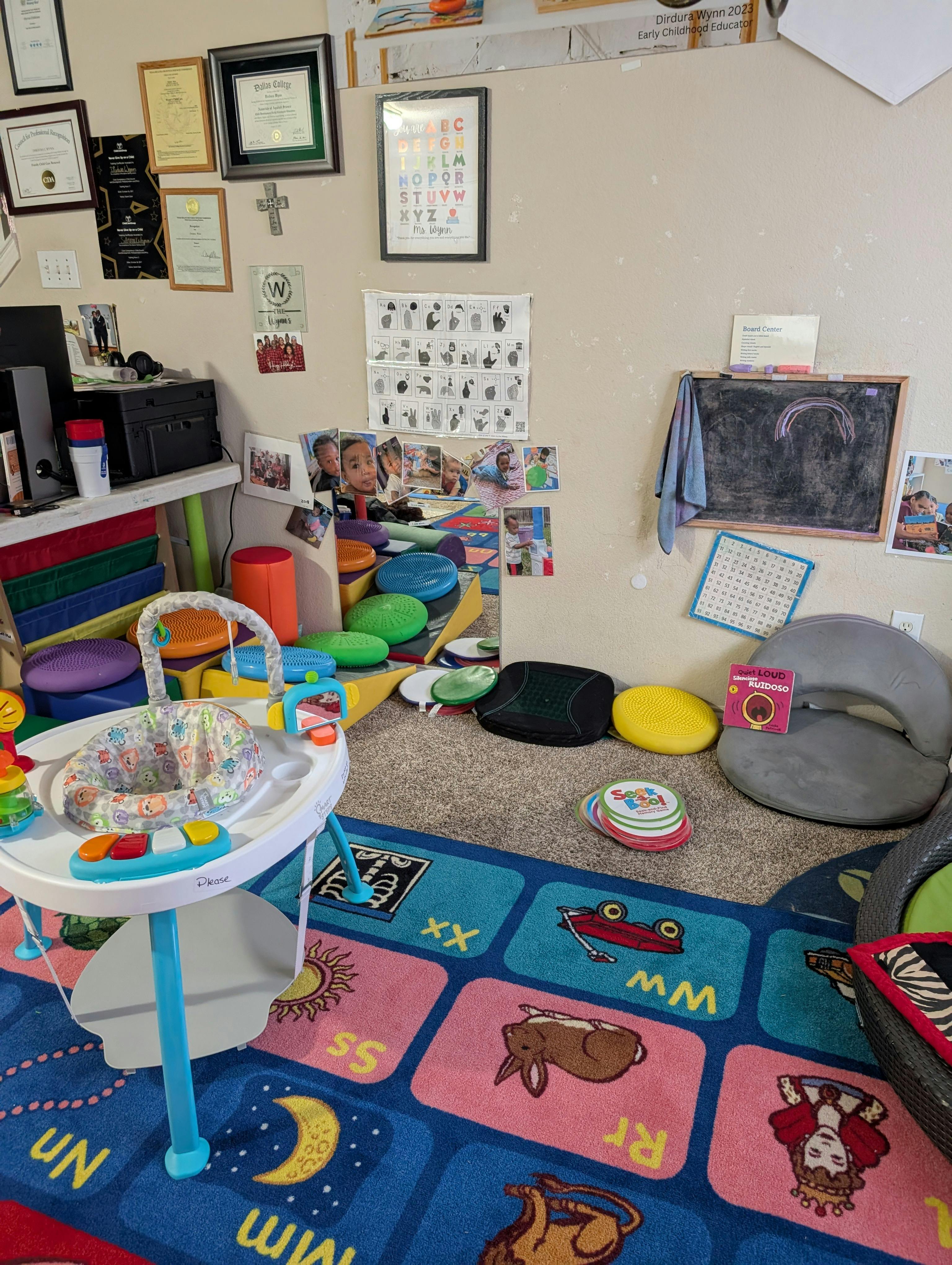 Childcare room with a play mat, infant bouncer, blackboard, and colorful floor cushions