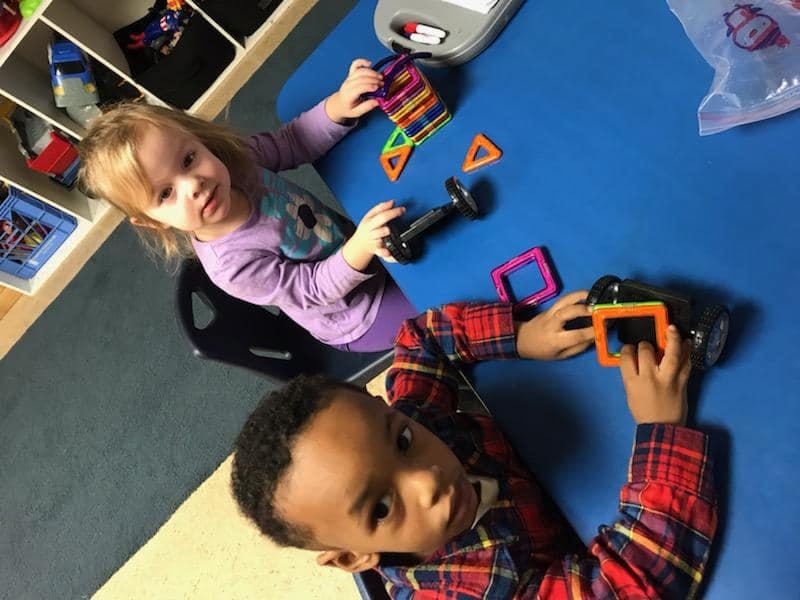 Two children playing with magnetic building toys at a blue table