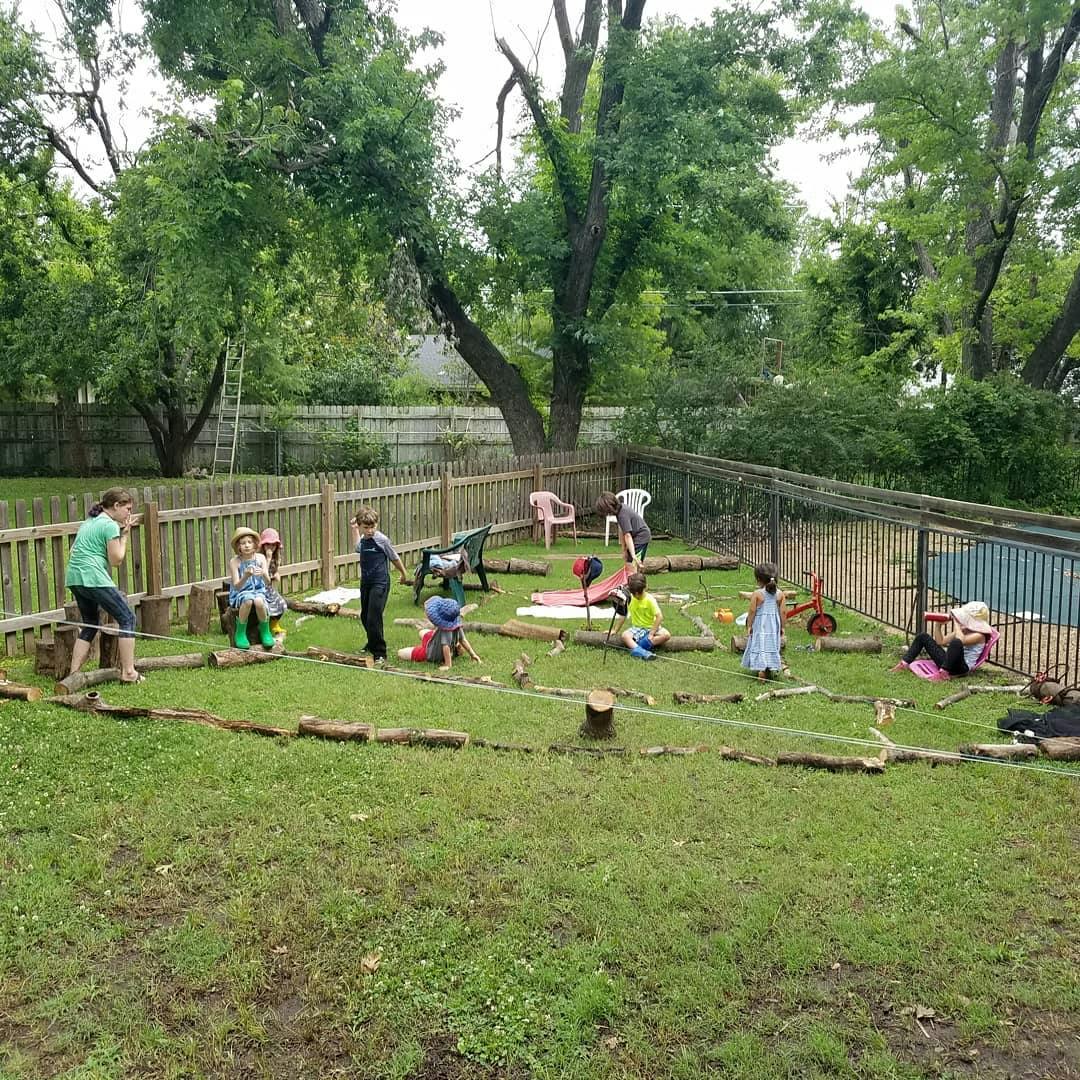 Children playing in a grassy backyard with logs and other items