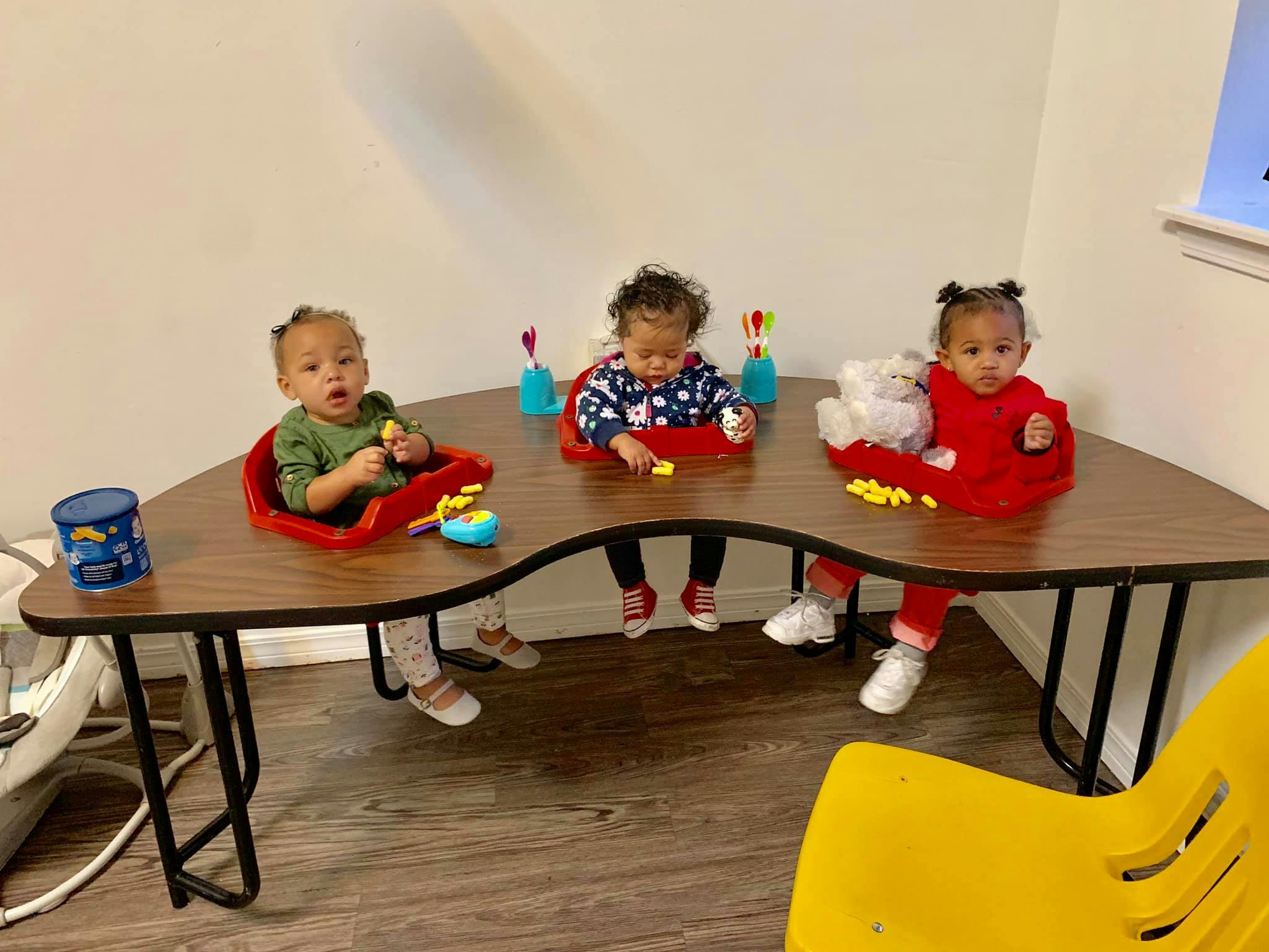 Three children sitting at a curved table with toys