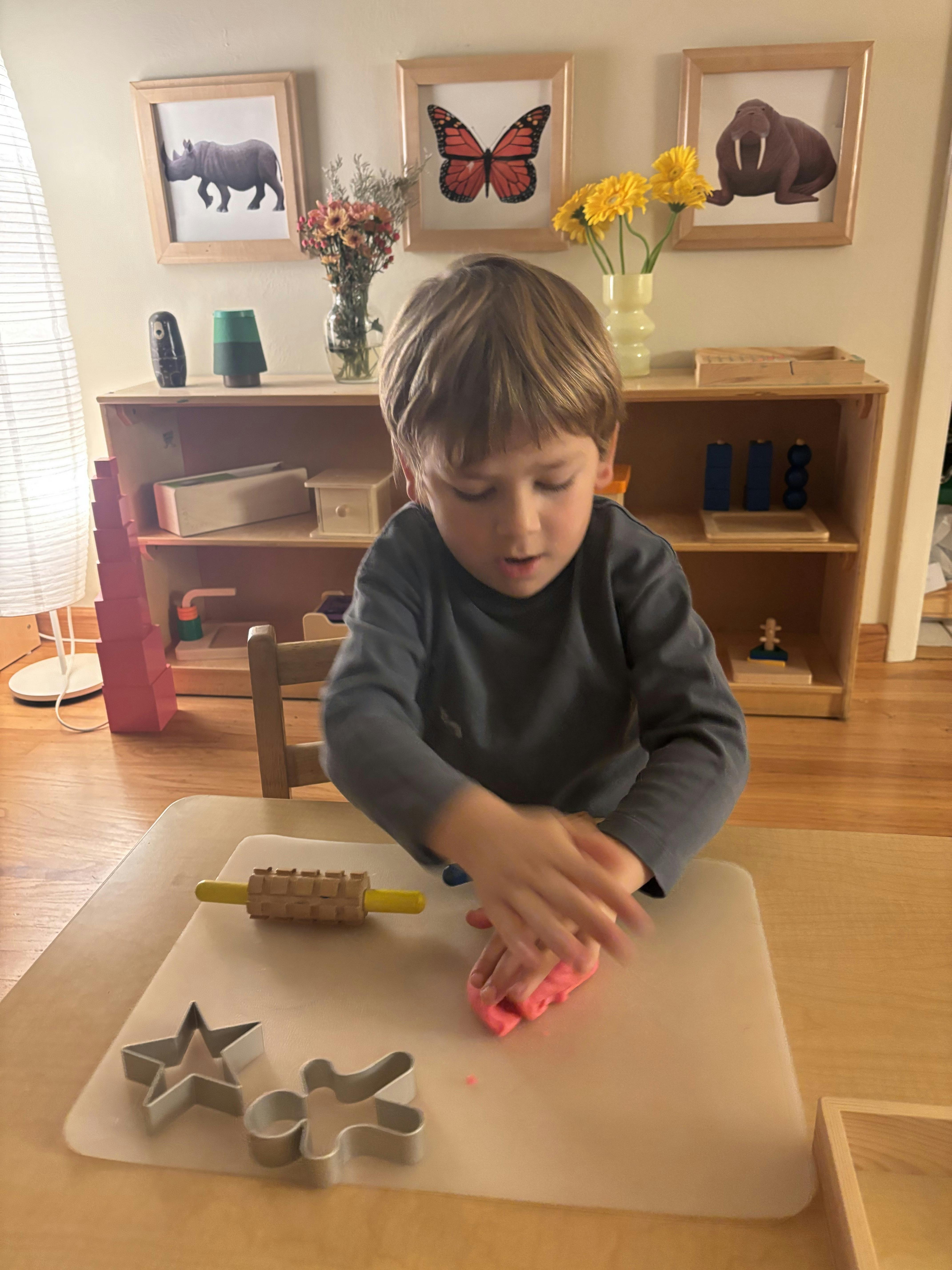 Child playing with pink dough on a table with cookie cutters