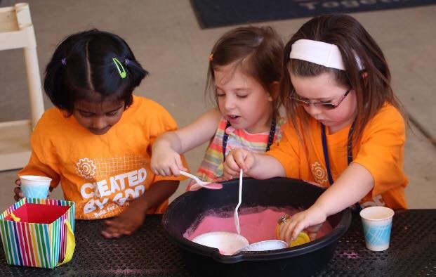 Three children playing with pink liquid in a black tub