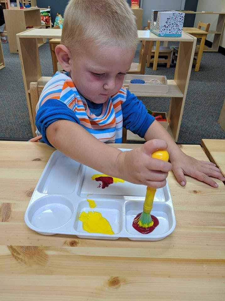 Child painting with a brush and paint tray in a classroom