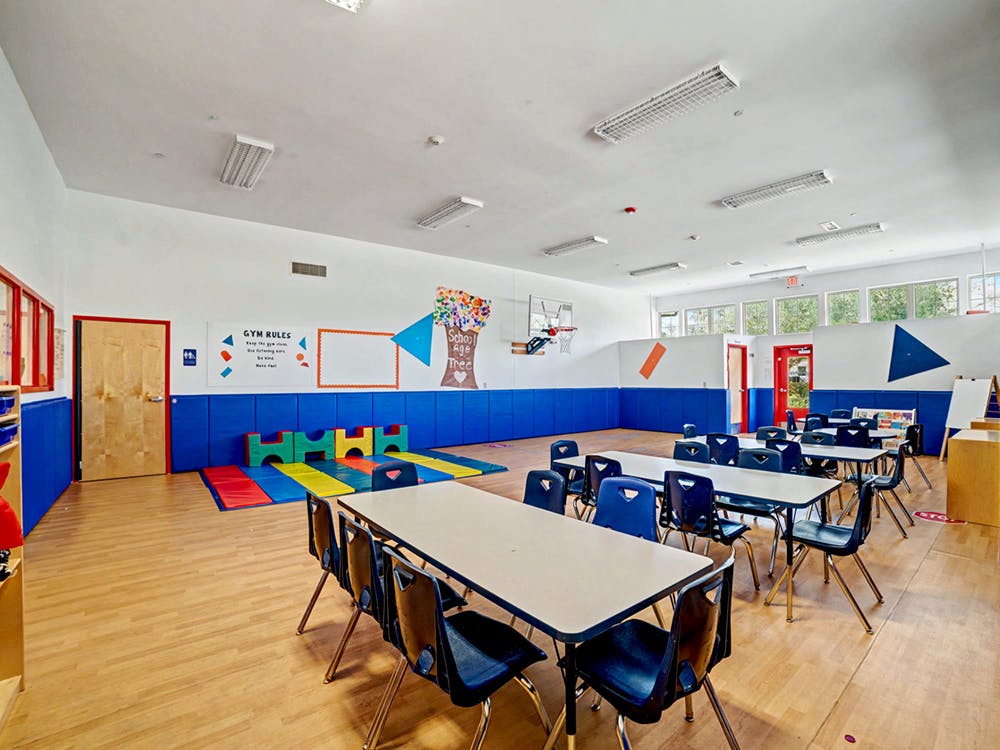 Classroom or play area with small tables, chairs, and gym mats