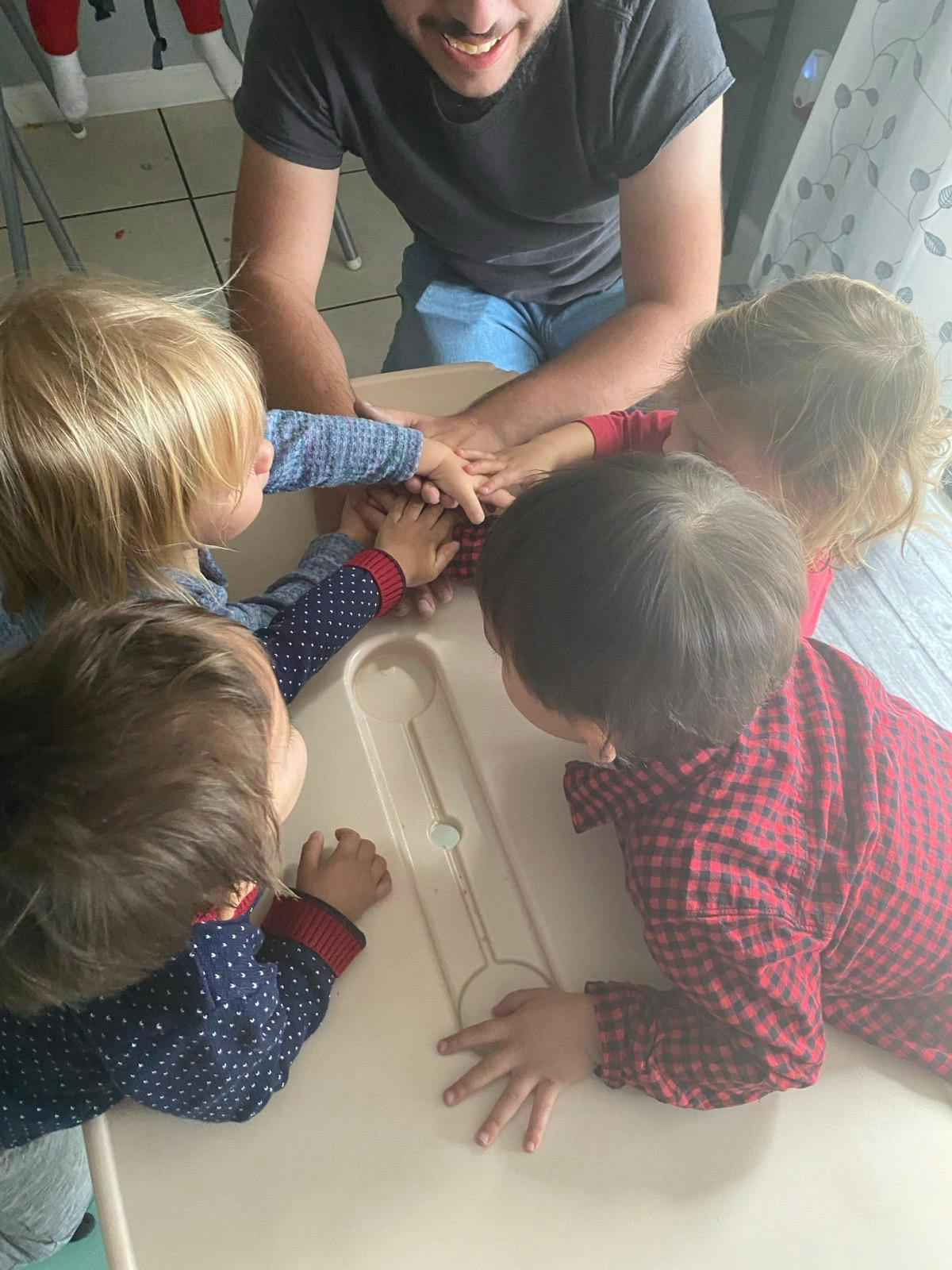 Person and three children with hands stacked on a table