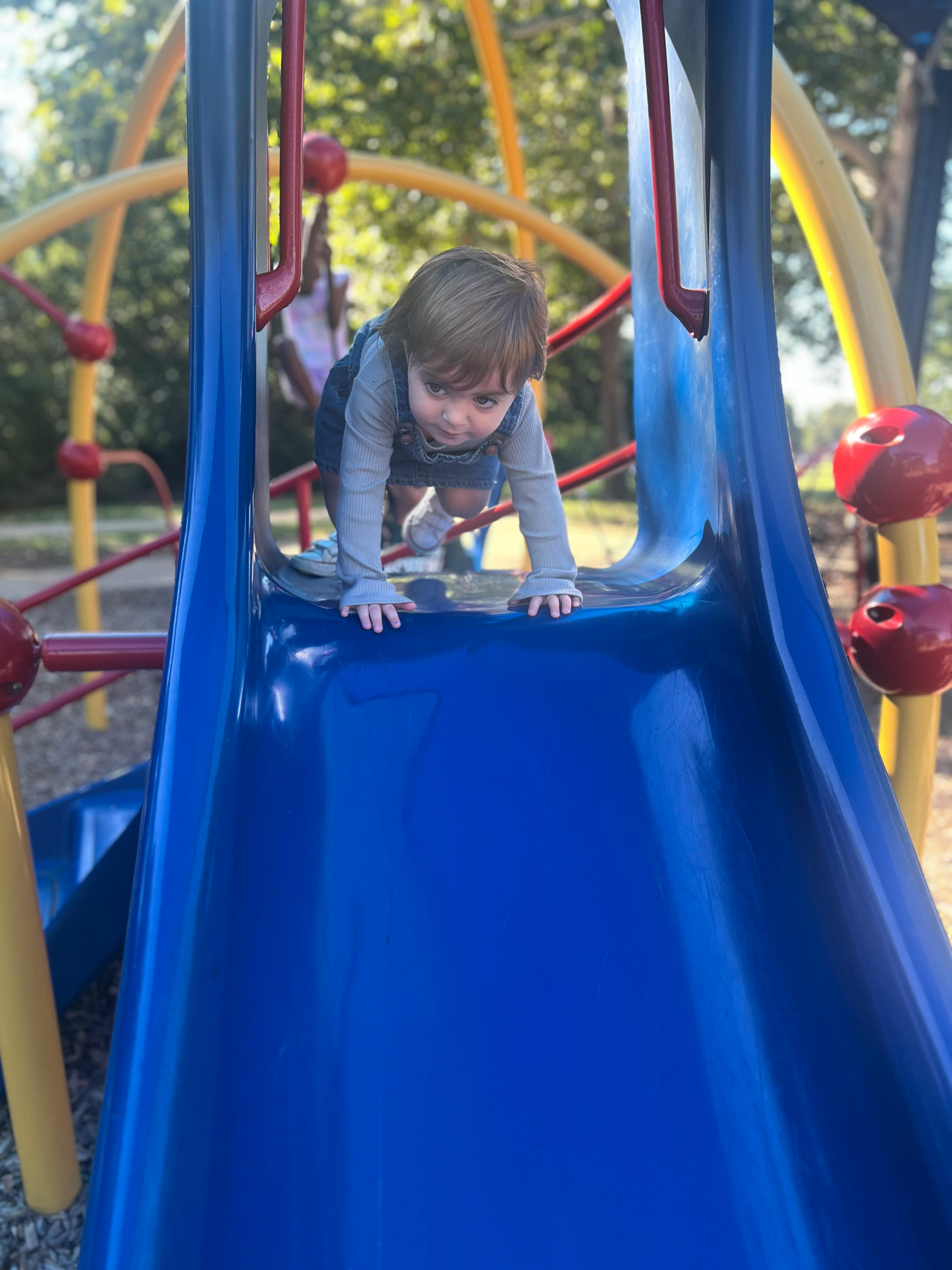 Child on hands and knees at the top of a blue slide on a playground