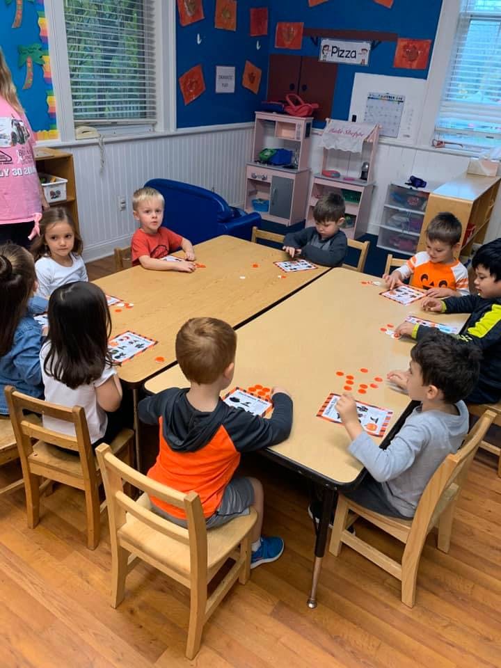 Children sitting at tables in a classroom, playing a game with small orange pieces