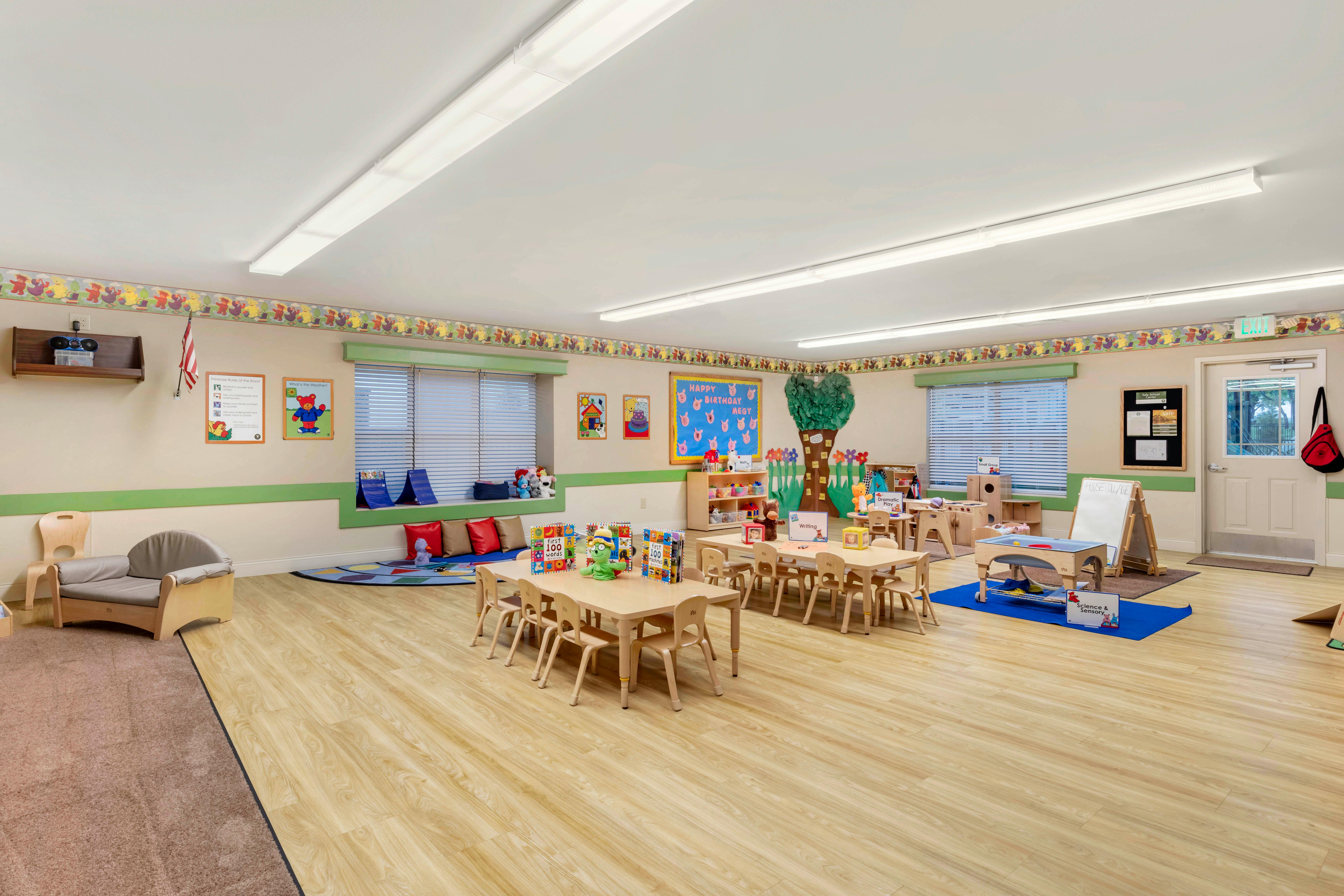 Classroom with small tables and chairs, window seat with pillows, and a tree decoration