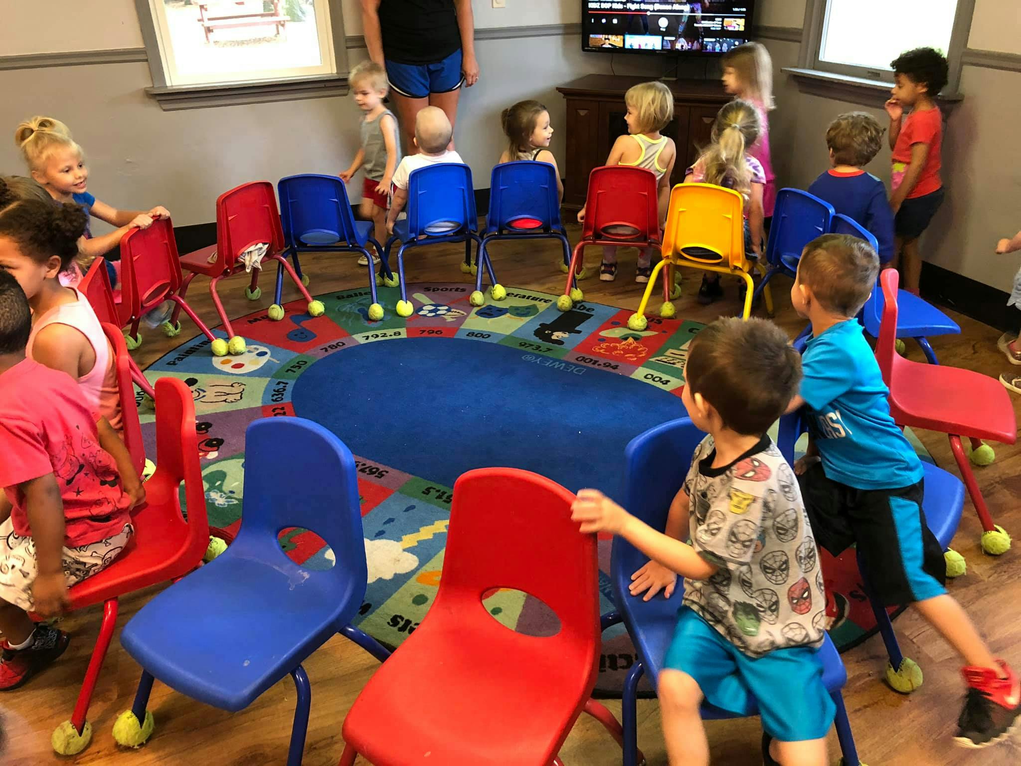 Children and adults in a room with small chairs arranged in a circle