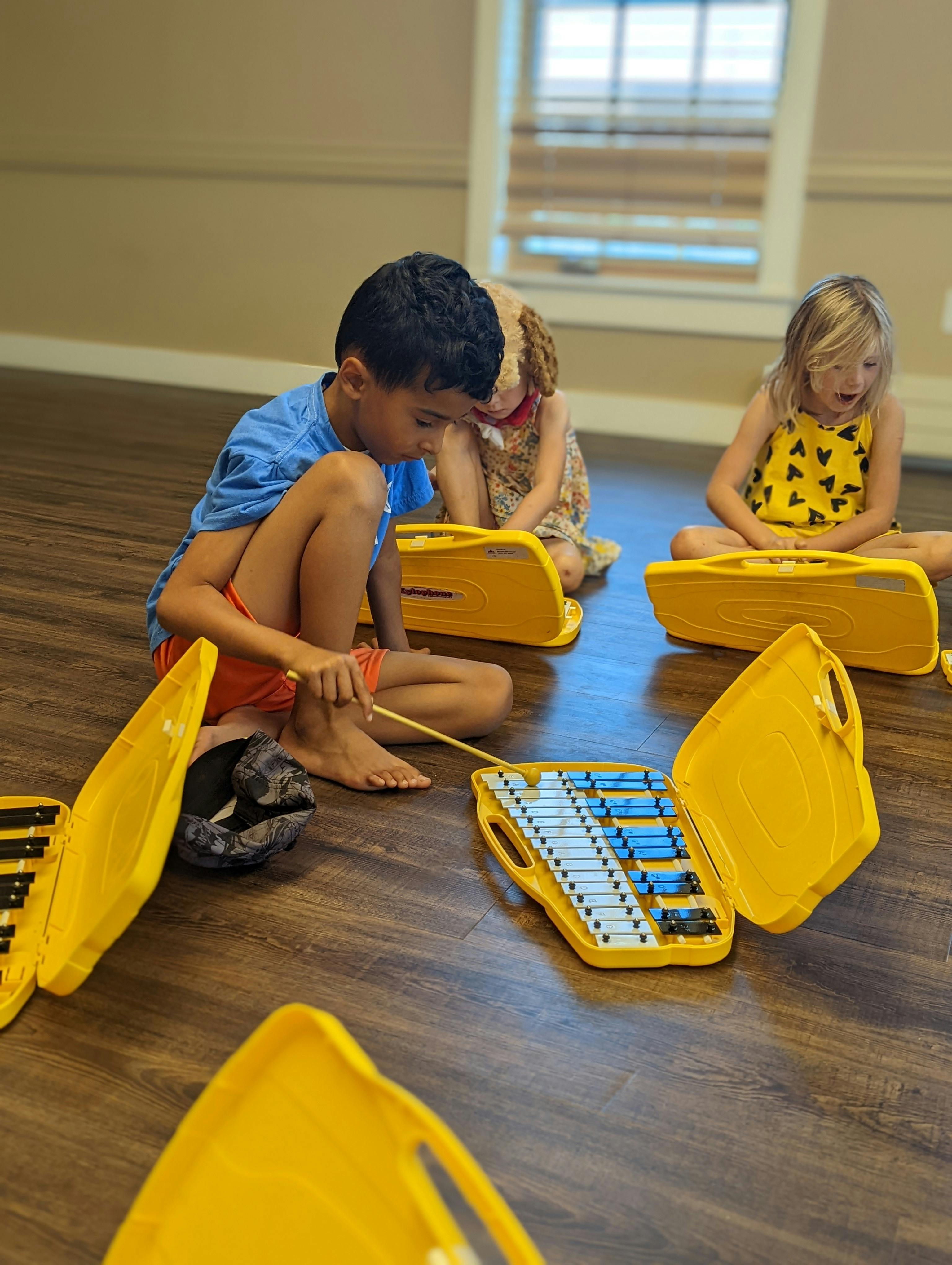 Child playing a xylophone on the floor with other children