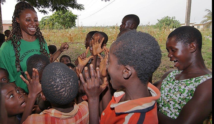 Smiling person in green shirt with children making hand gestures