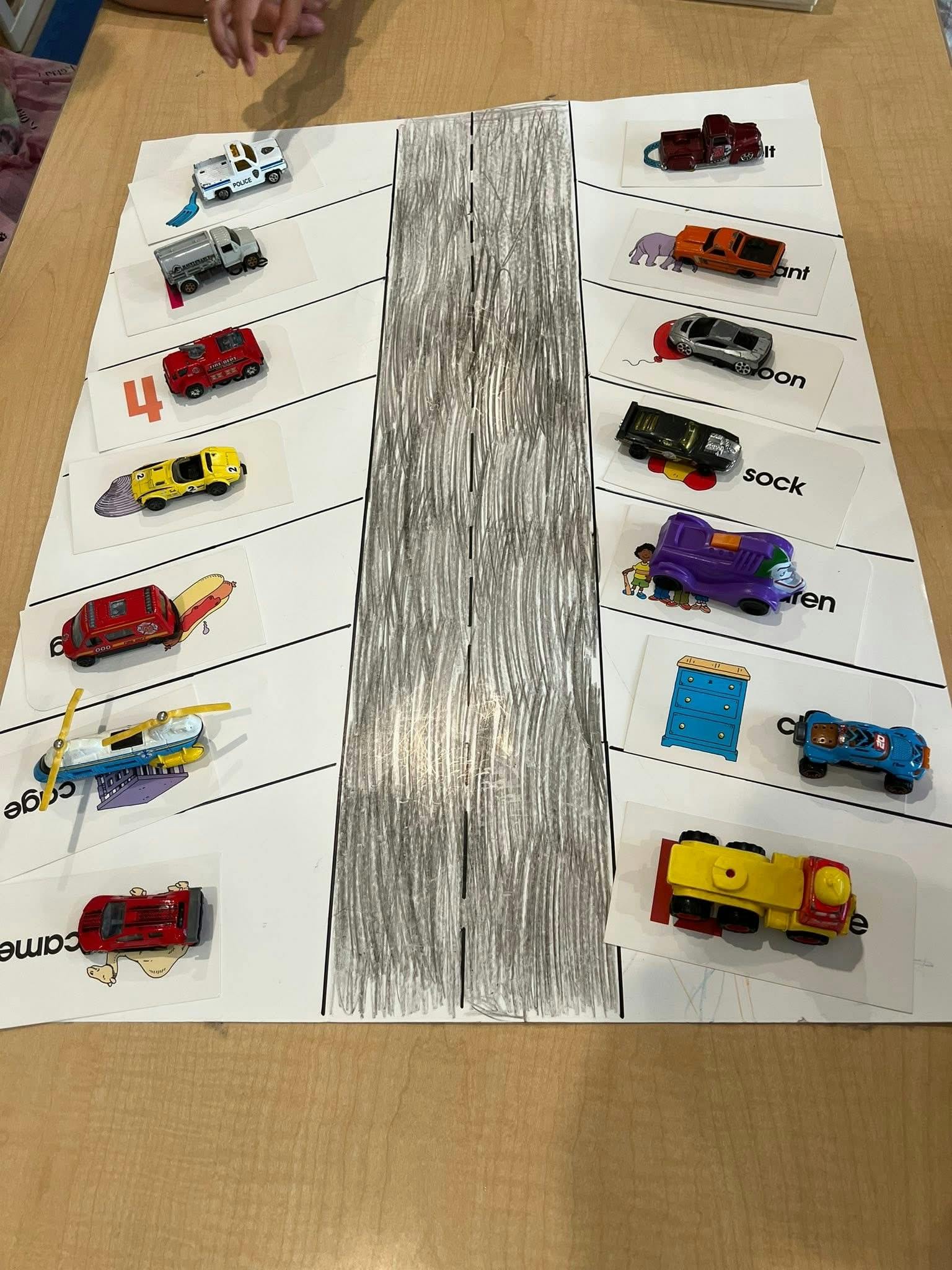Toy cars parked on paper cards with images and words along a hand-drawn road