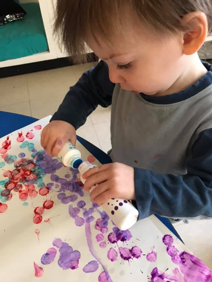 Child painting with two bottles of paint on paper