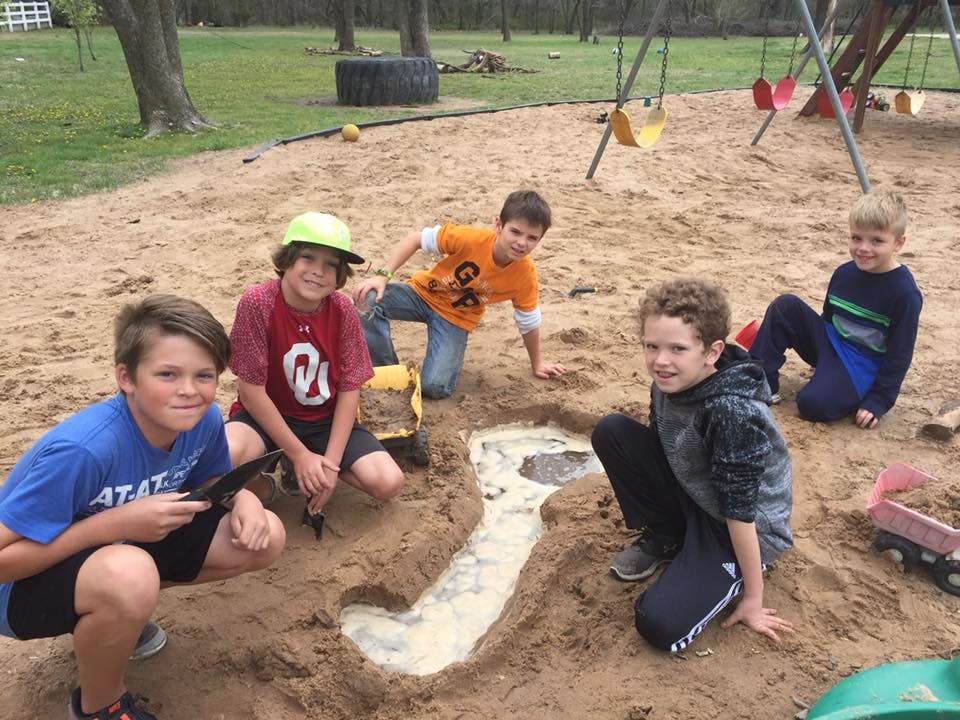 Five children playing in a sandbox with a water-filled trench