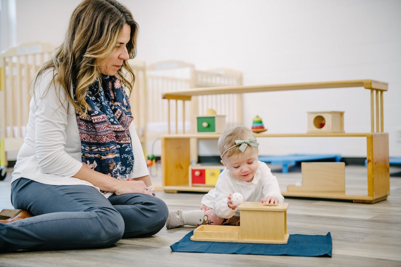 Person observing a child playing with a wooden toy on the floor