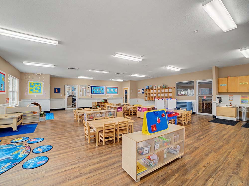 Empty preschool classroom with small wooden tables and chairs