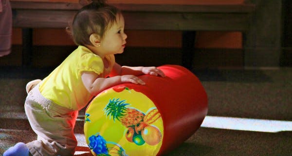 Child on knees with hands on a red and yellow toy