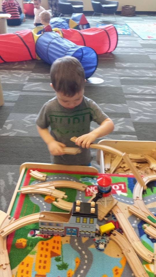 Child playing with a wooden train set on a rug