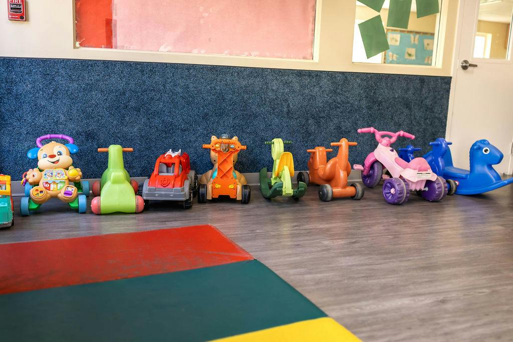 A line of colorful toddler ride-on toys against a wall in a room