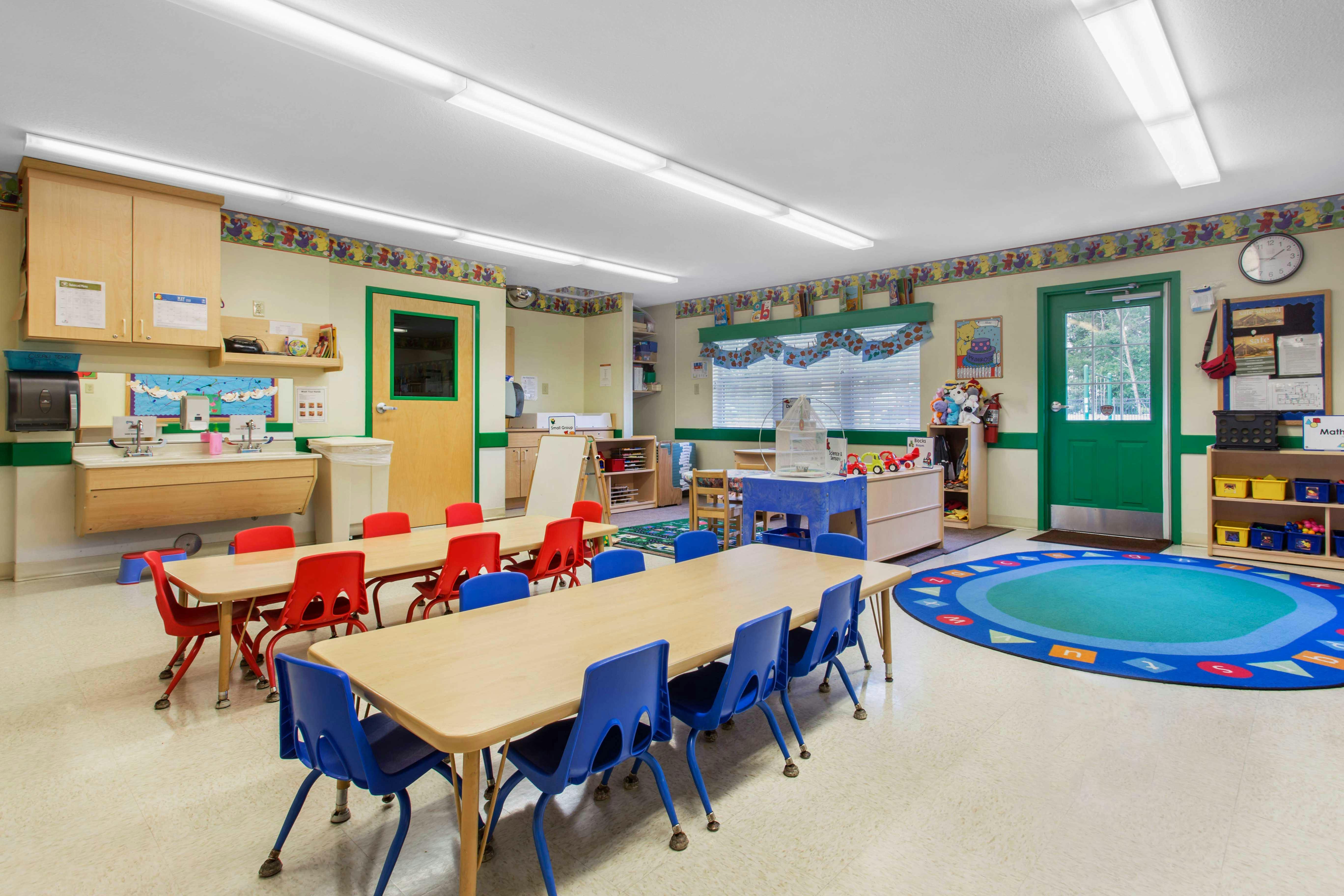 Classroom with small tables and chairs, a sink, and a round rug