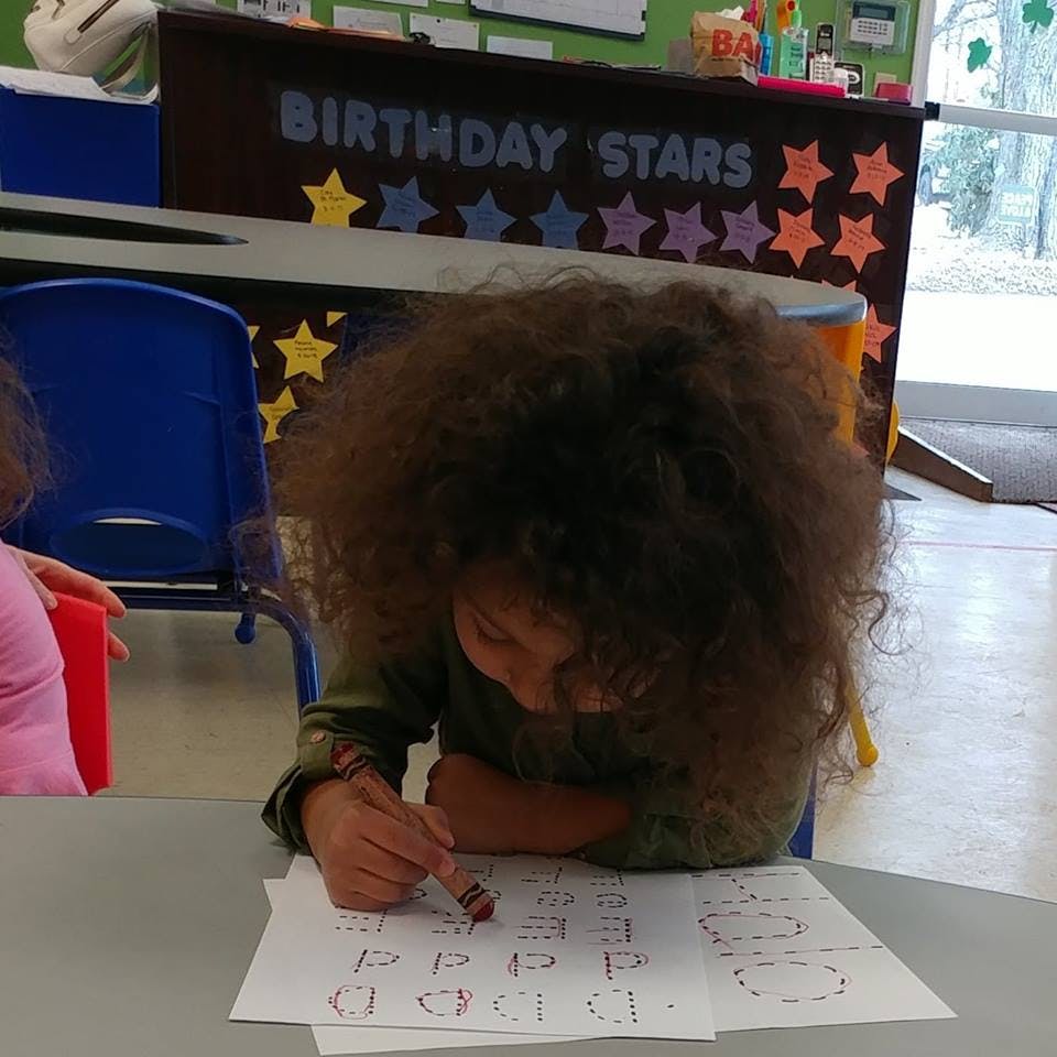 Child tracing letters on a worksheet in a classroom