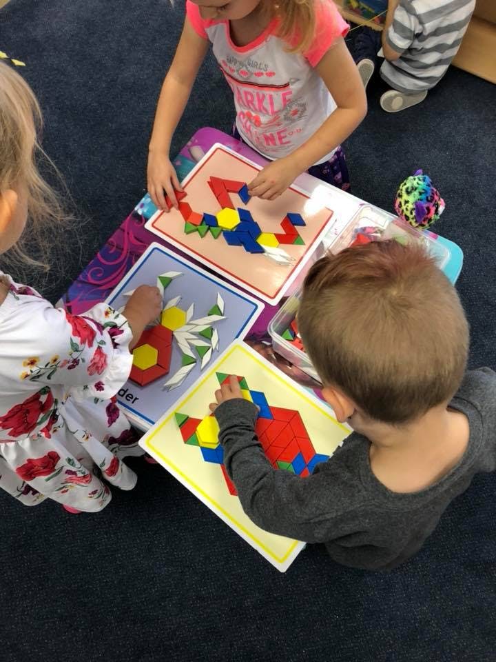 Three children playing with colorful pattern blocks on a table