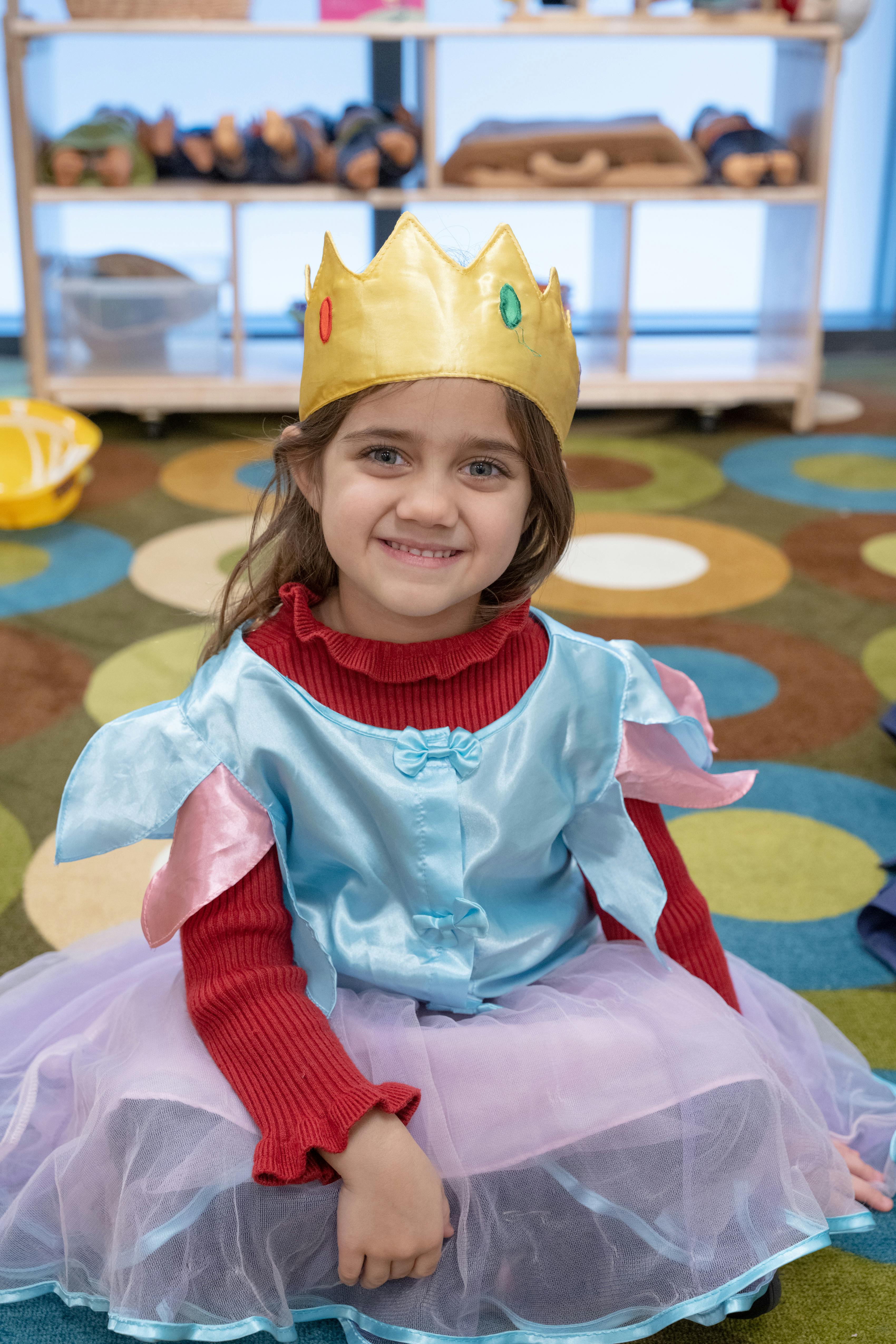 Child wearing a gold crown and a blue and red dress