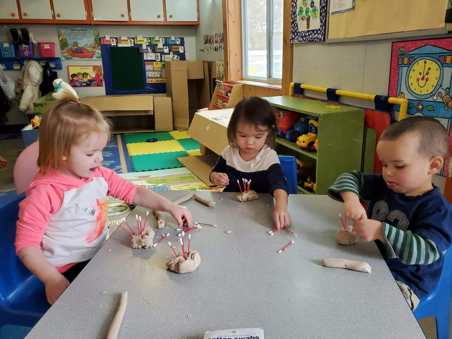 Three children playing with modeling clay at a table in a classroom
