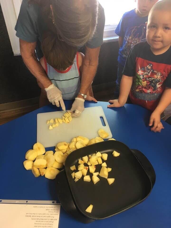 Adult and child cutting apples on a cutting board with other children watching