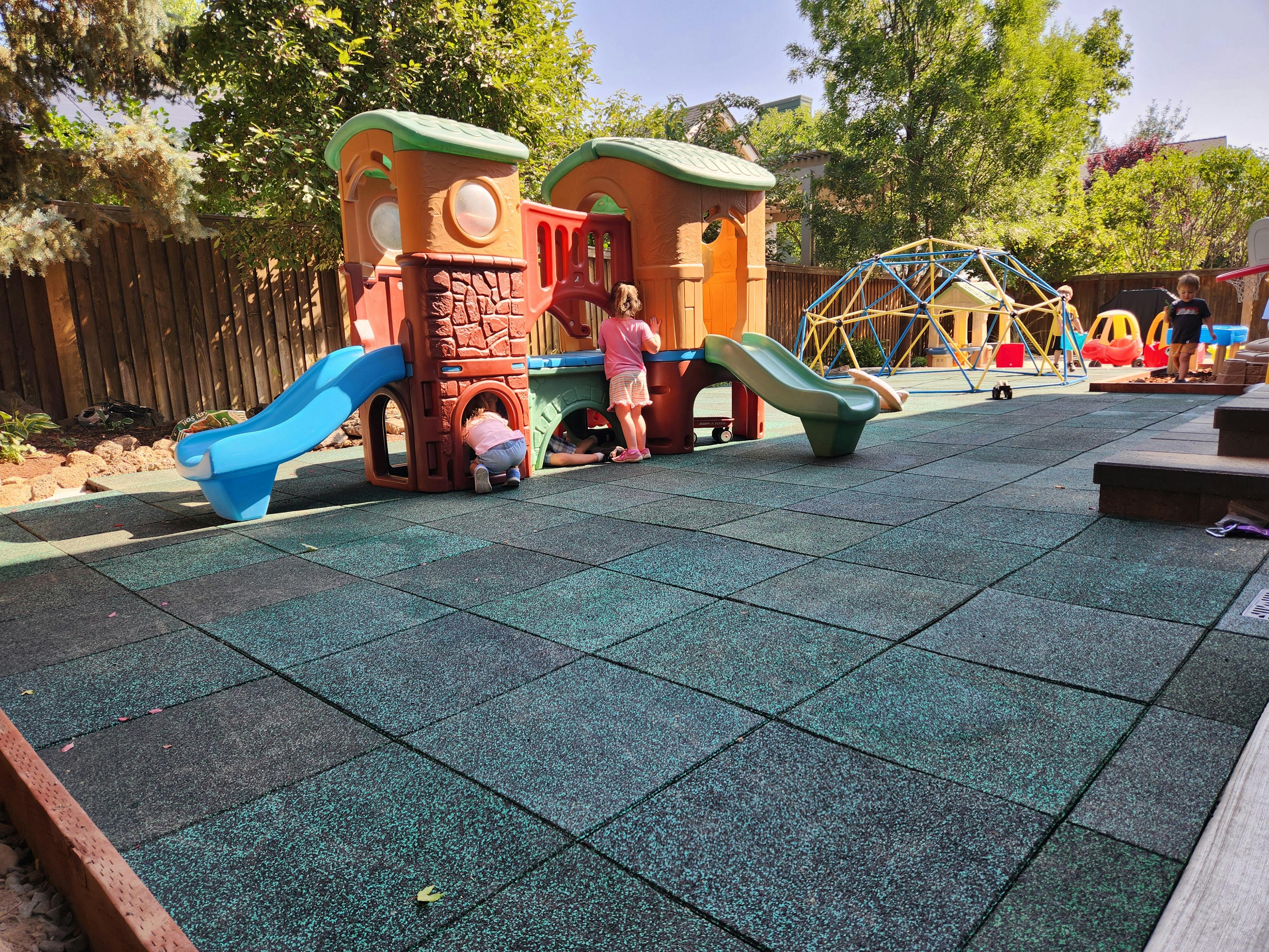 Child standing on a playground structure with another child crawling inside