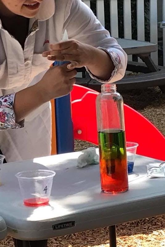 Person in lab coat pouring liquid into a bottle with layered liquids