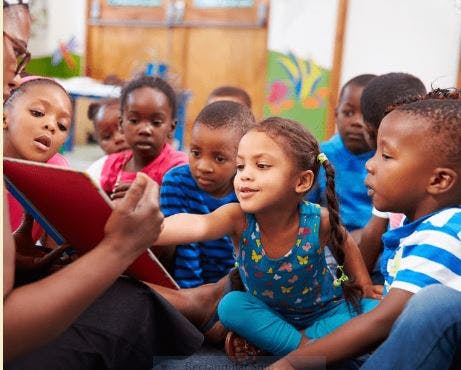 Adult reading a book to a group of children in a classroom