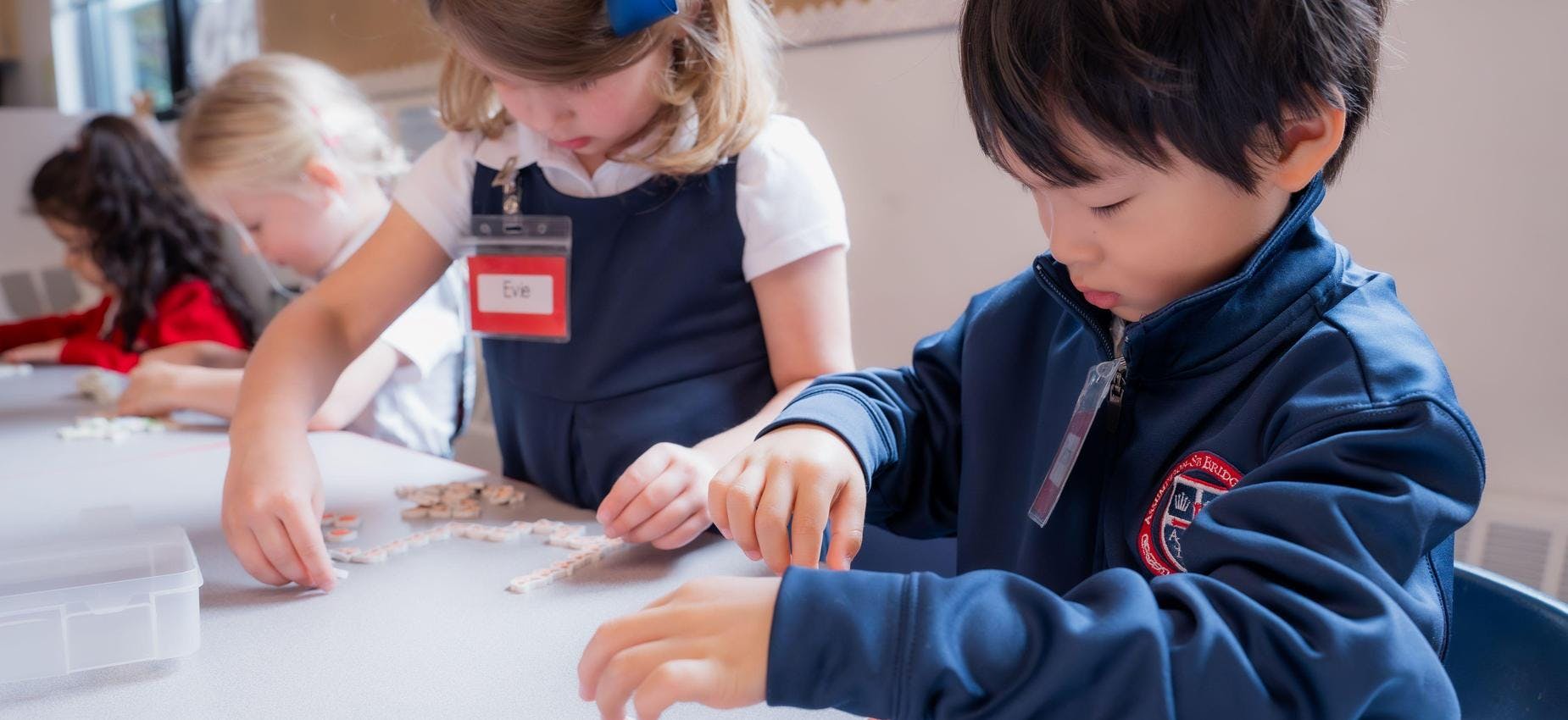 Children playing with letter tiles at a table in a classroom
