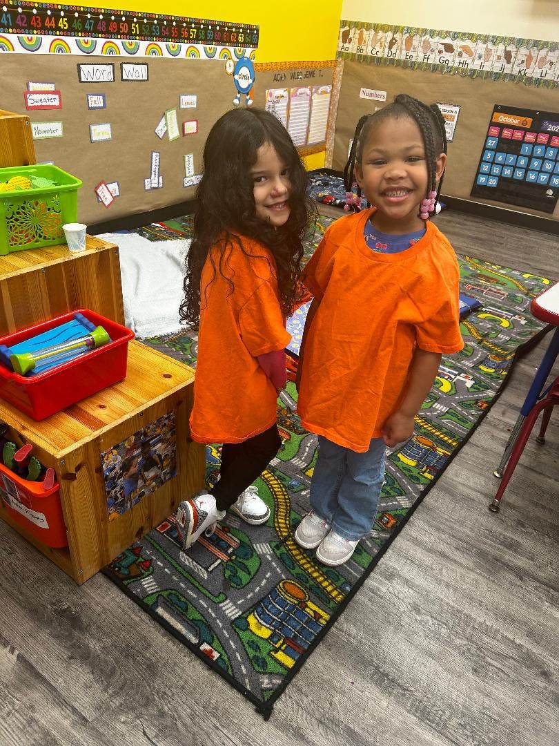 Two children standing on a road-patterned rug in a classroom